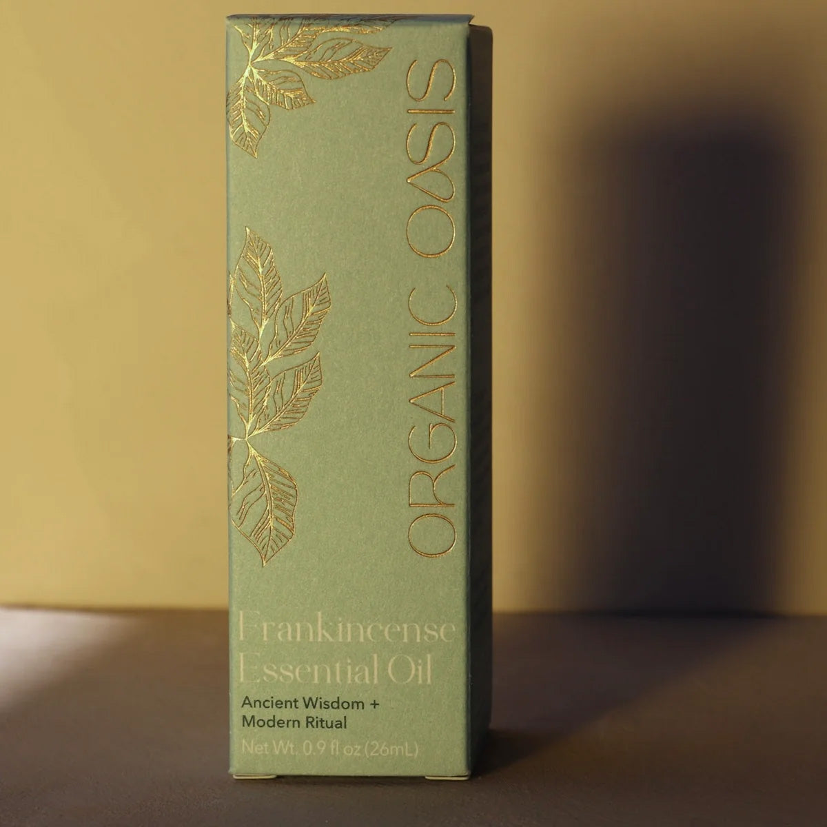 Box of Organic Oasis Frankincense Essential Oil with gold leaf designs on a brown background