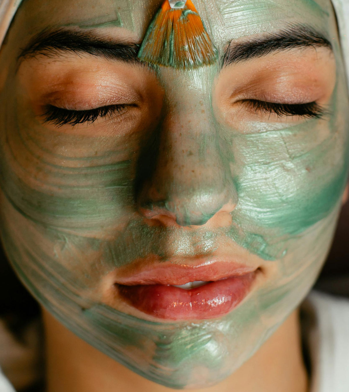 Person applying a green facial mask to their face with a brush.