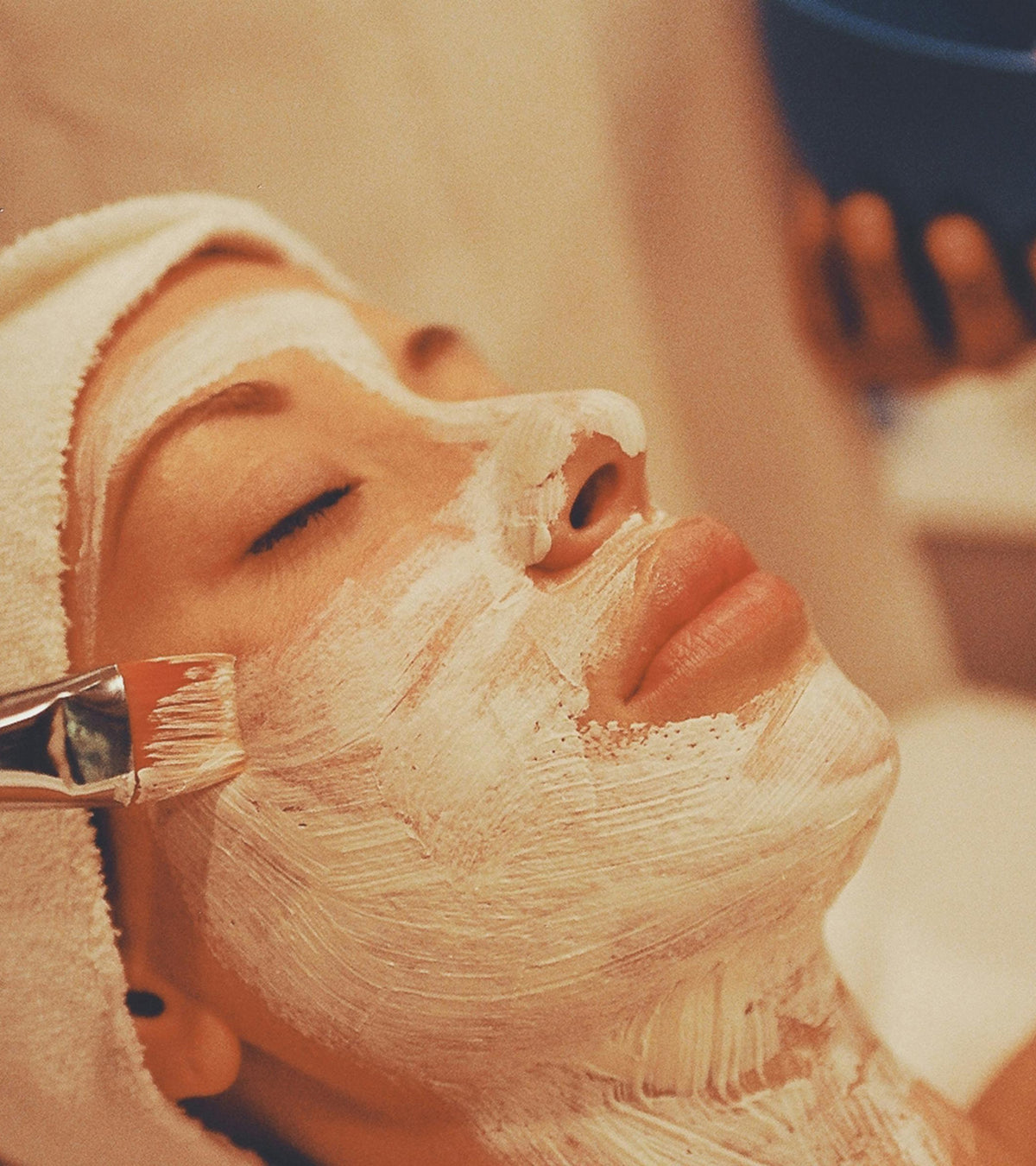 Person receiving a facial with a brush applying cream to their face.